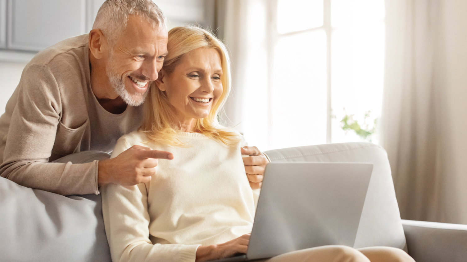 A woman sat with her husband behind her looking at a laptop smiling