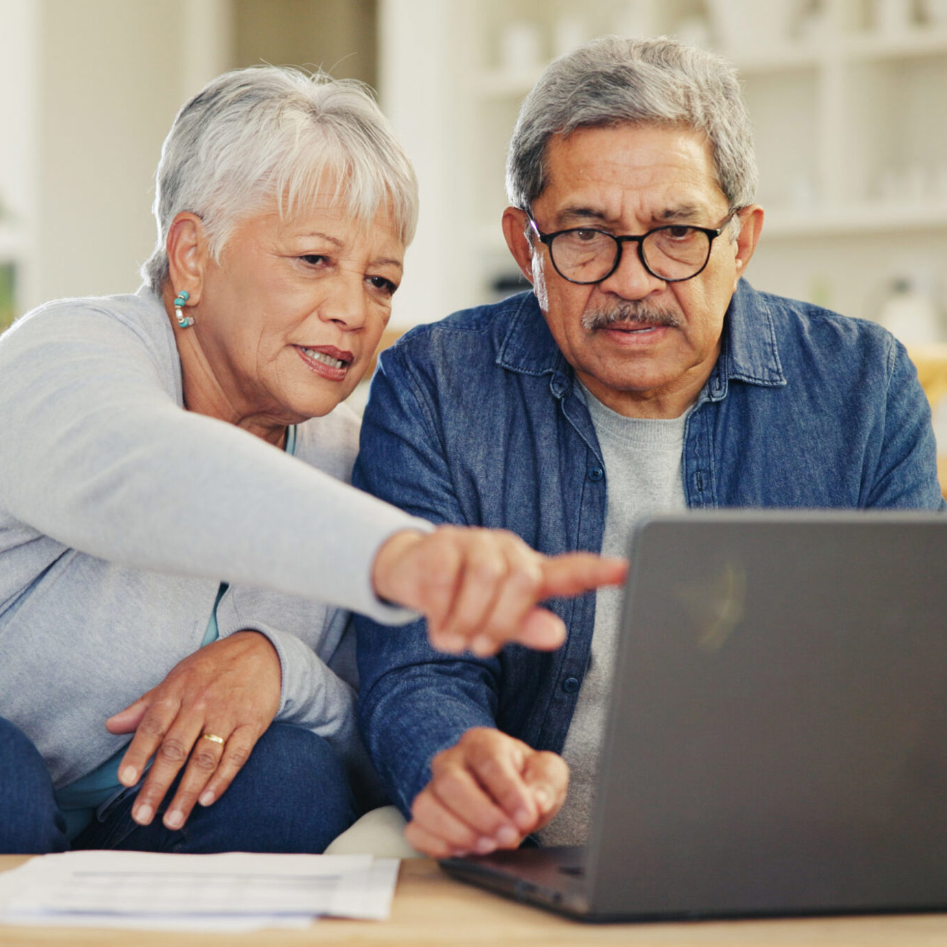Senior couple sitting together on a sofa, smiling and looking at a laptop at home.
