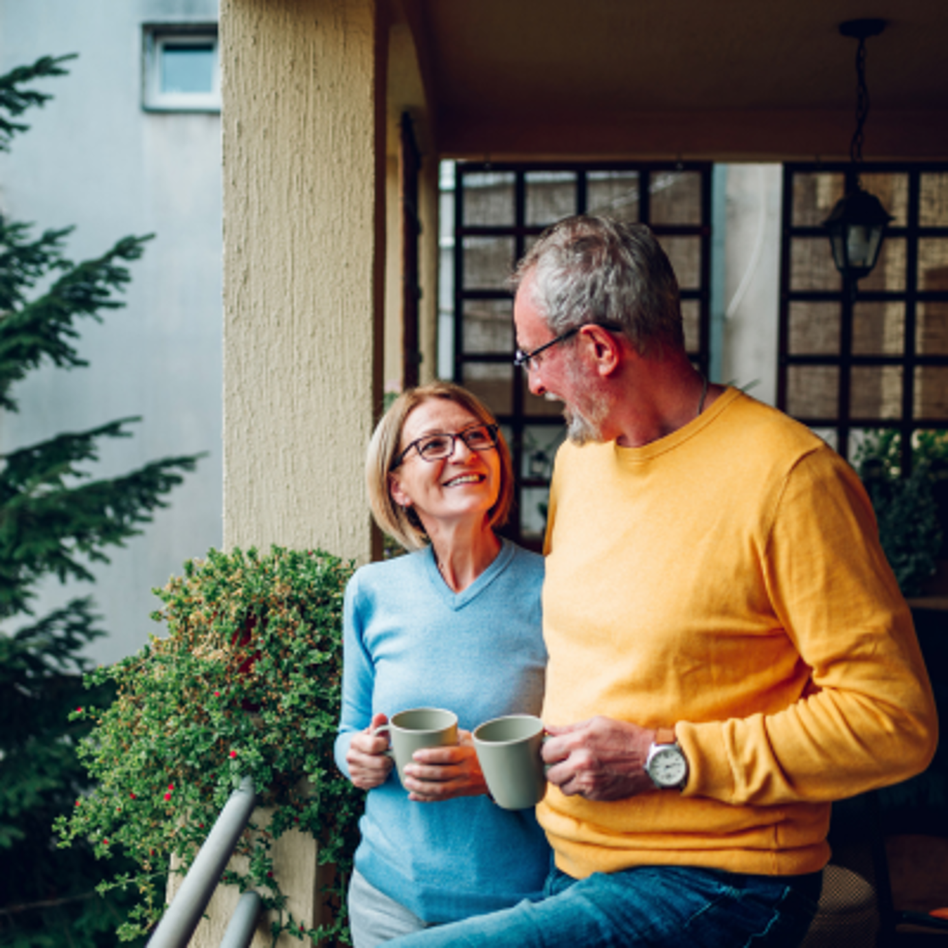 Smiling senior couple standing together outside their home, enjoying a happy moment.