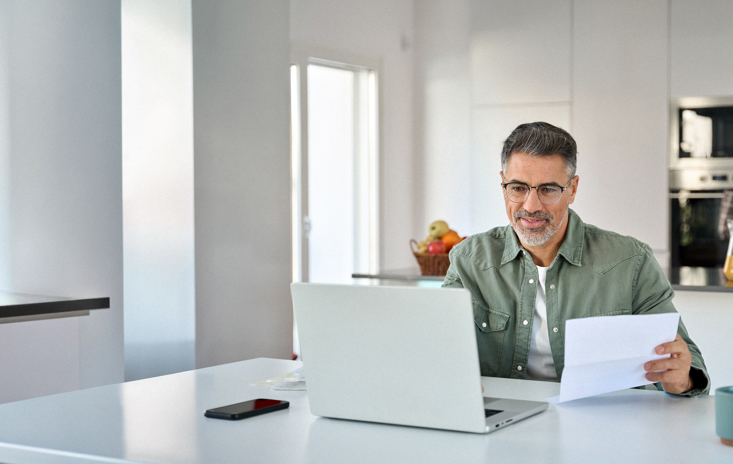 Senior male alone sat, looking and smiling at his laptop