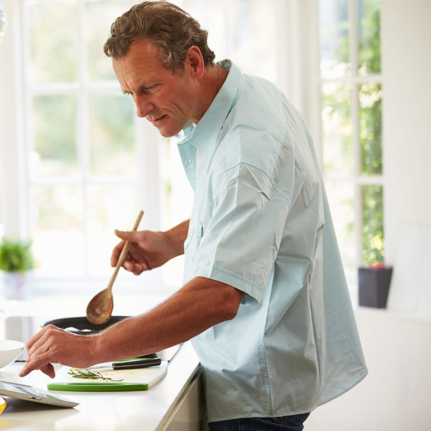Mature man preparing a meal in a bright kitchen at home.