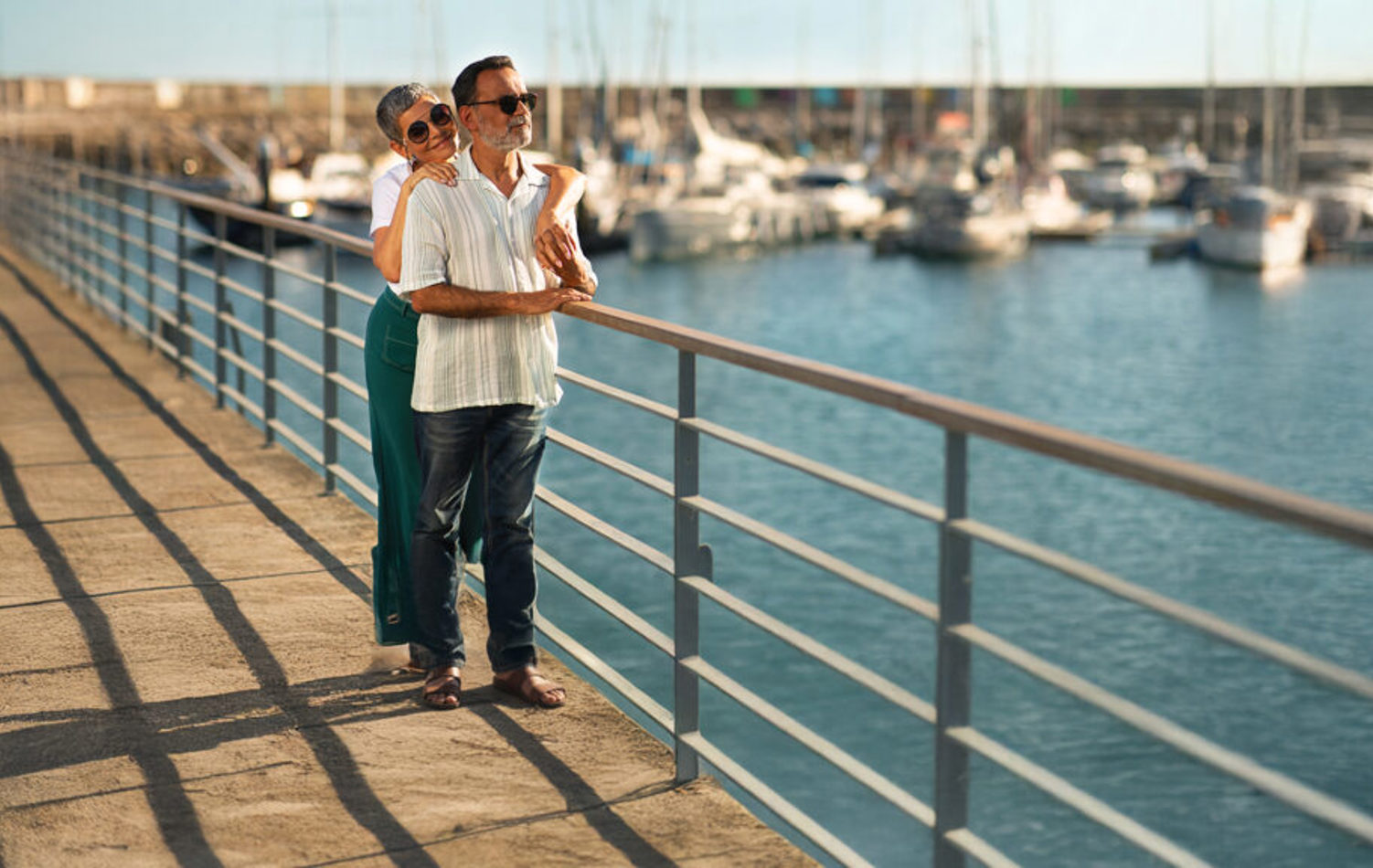 A senior couple stood on a pier looking out to see in the bright sunshine